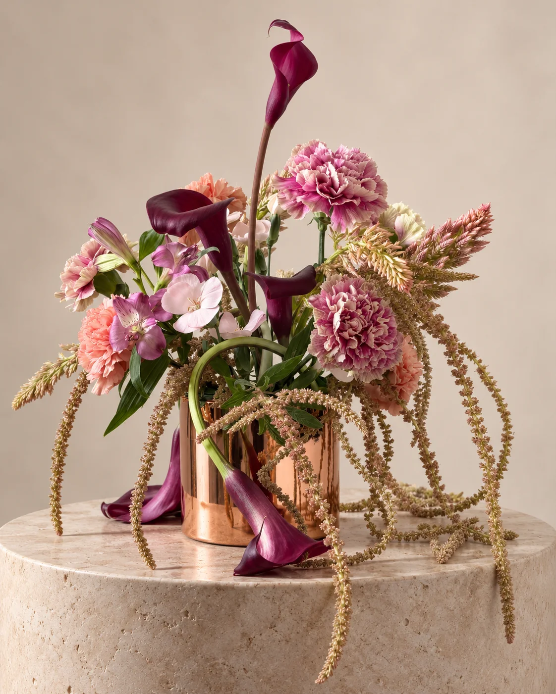 Burgundy calla lilies, pink flowers and trailing amaranth in a copper vase on pale stone
