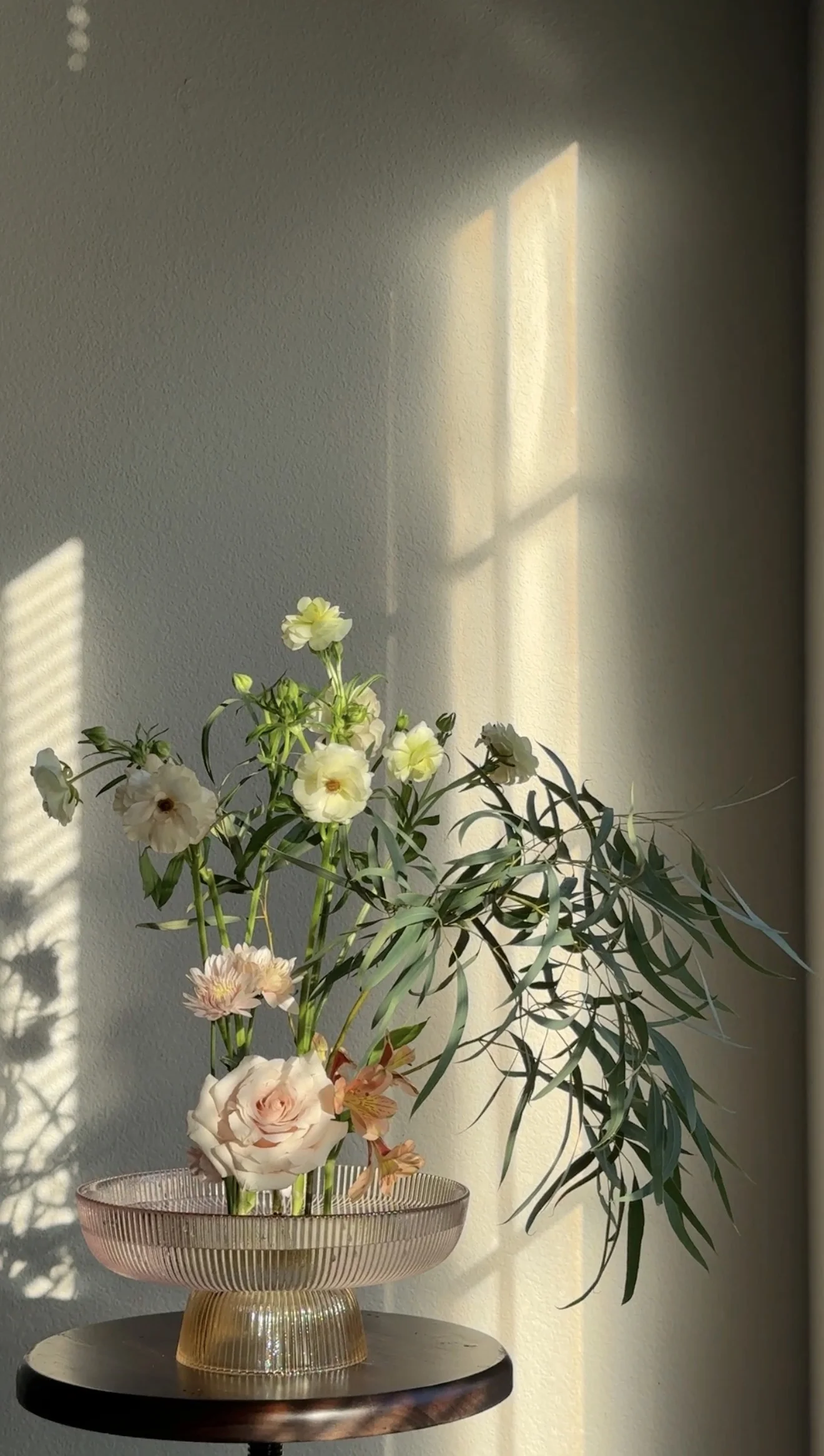 An airy arrangement of pale flowers and arching green foliage in a ribbed pedestal bowl