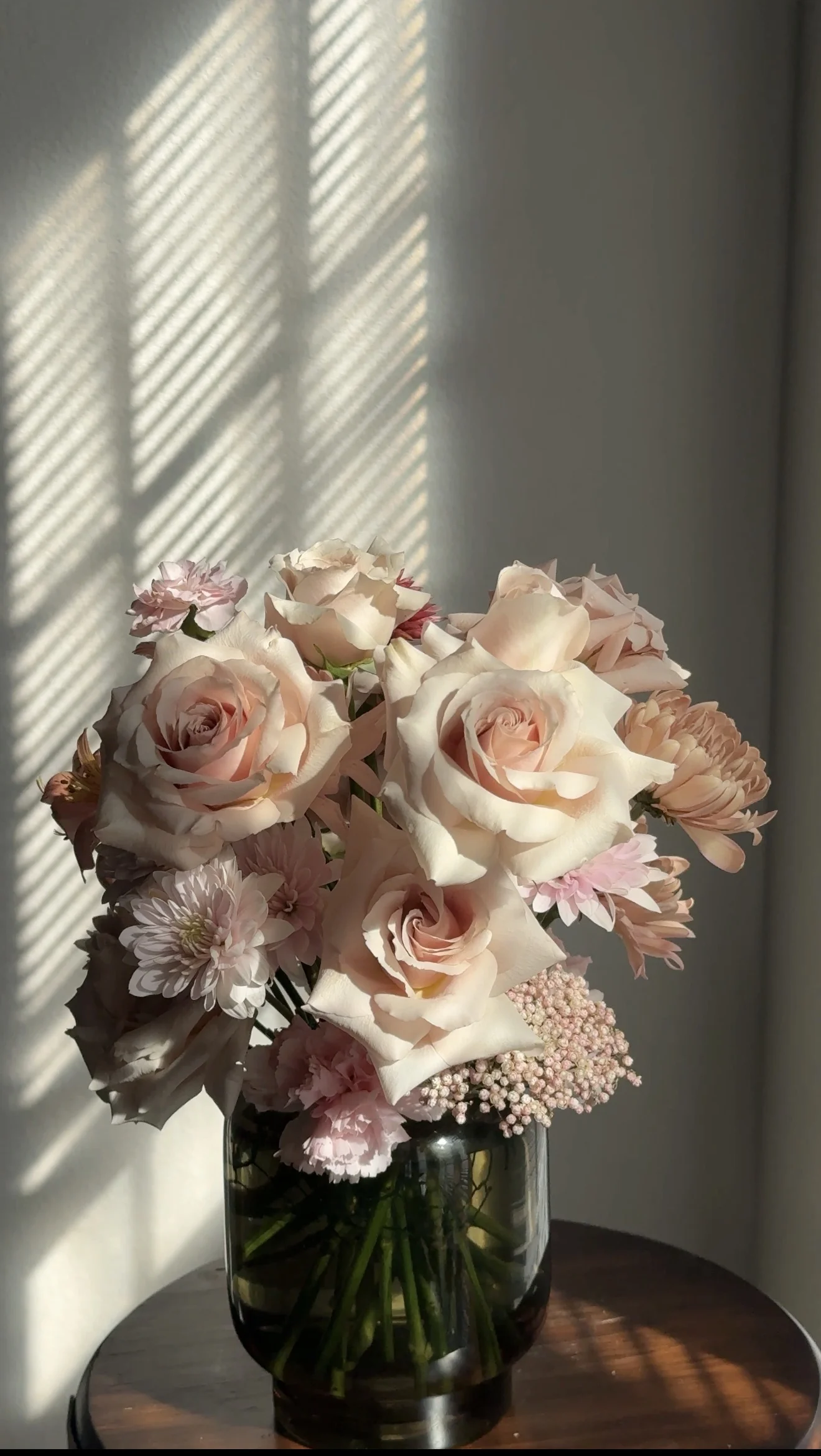 Blush roses and pink flowers in a green glass vase, in window light