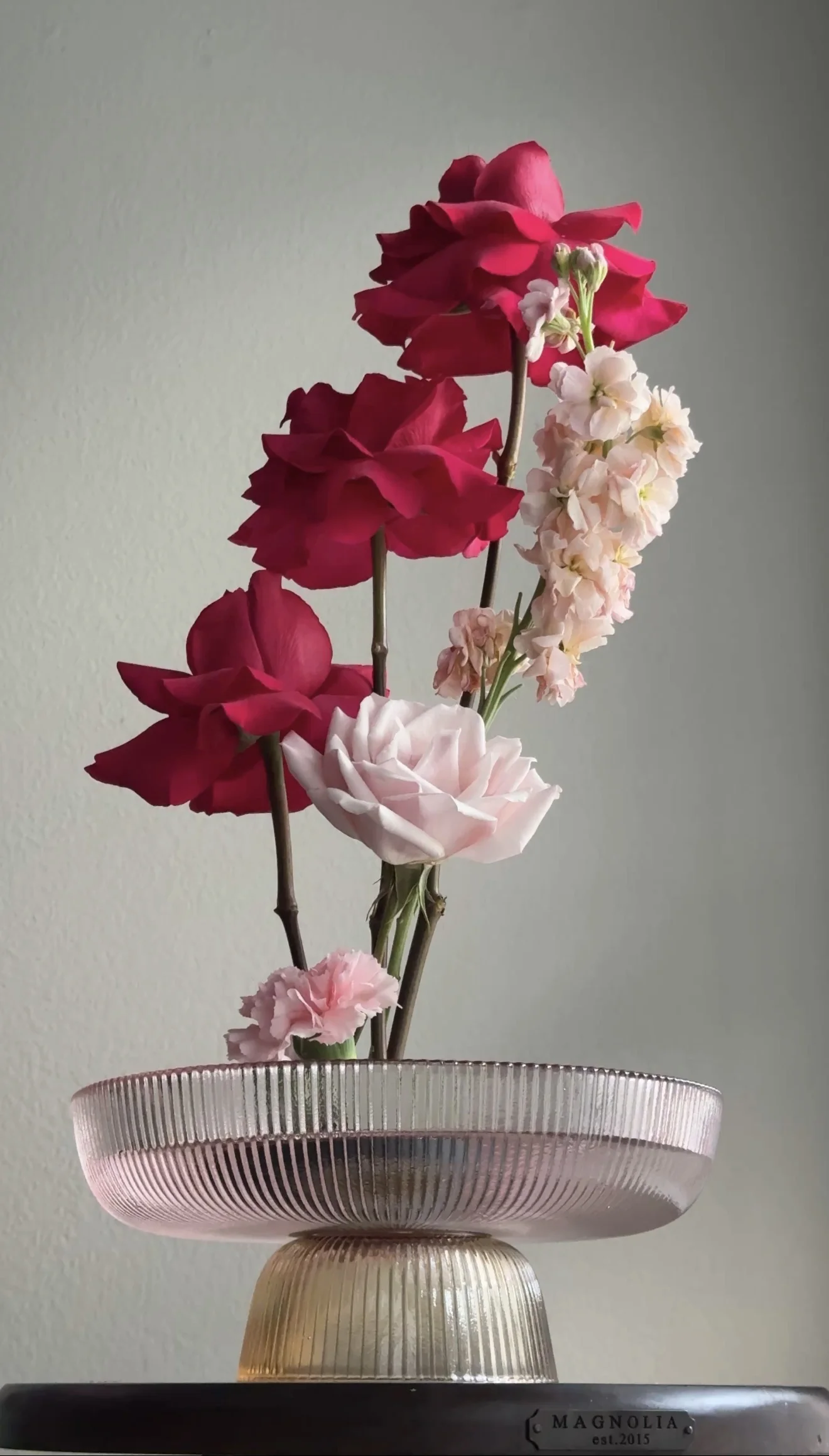 Red and blush roses arranged at different heights in a pink ribbed pedestal bowl