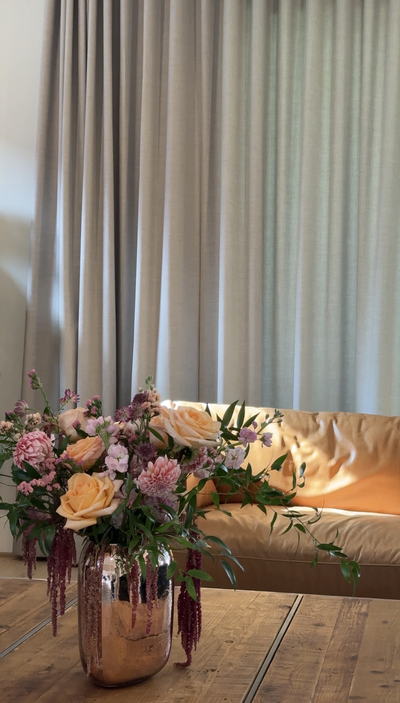 Peach roses and pink flowers with trailing burgundy amaranth in a copper-toned vase