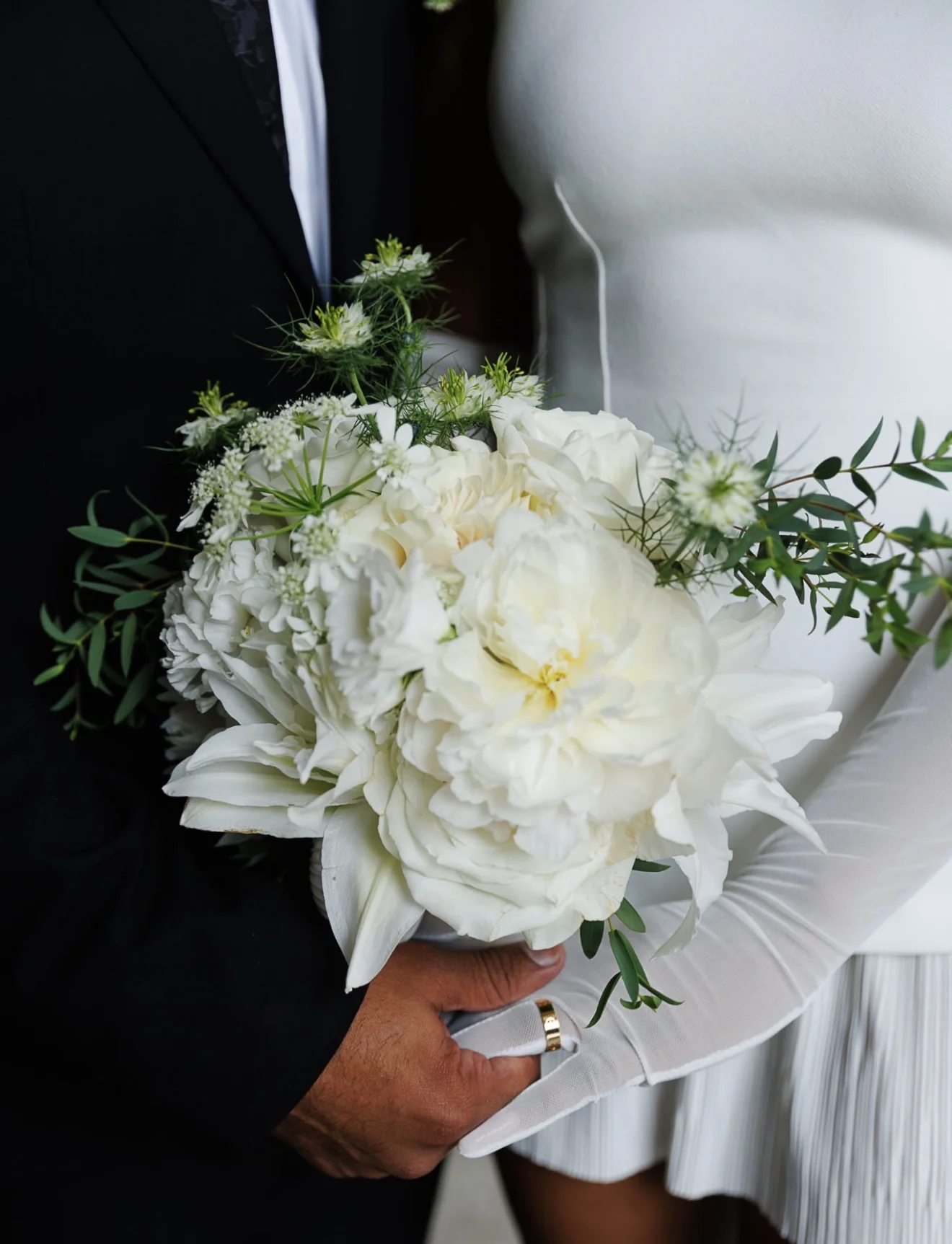 A couple holding a white bridal bouquet with fresh green foliage
